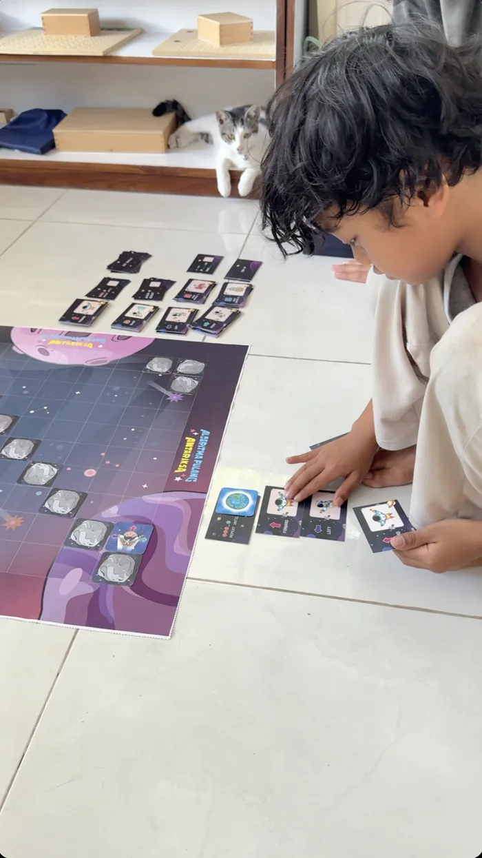 Anak duduk di lantai menyusun kartu perintah di papan permainan.